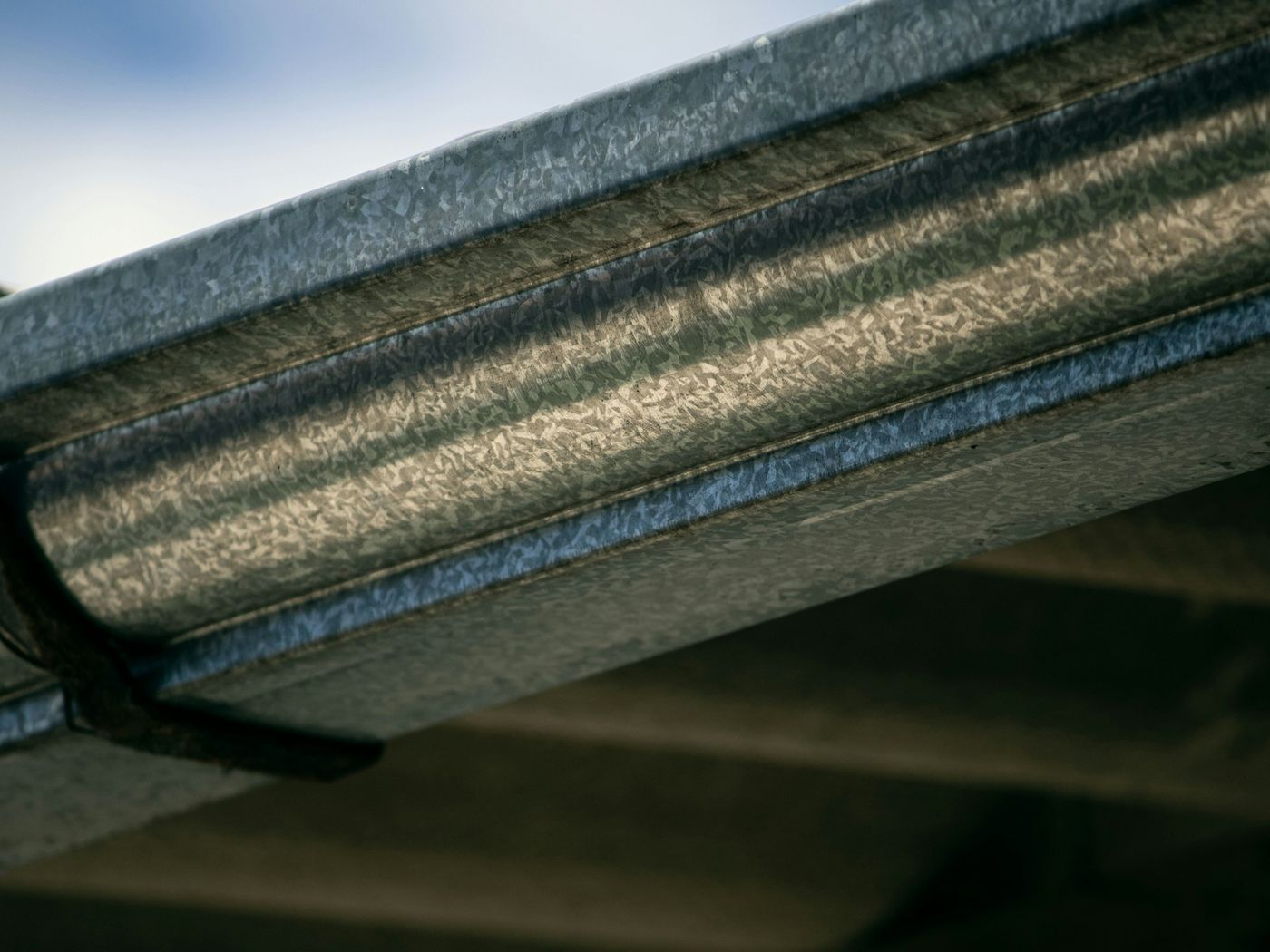 Backlit close-up along a galvanized metal gutter running under a roof edge